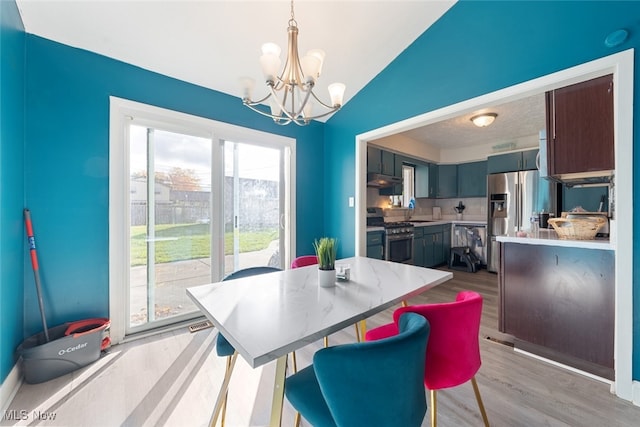 dining area featuring an inviting chandelier, light hardwood / wood-style flooring, sink, and vaulted ceiling