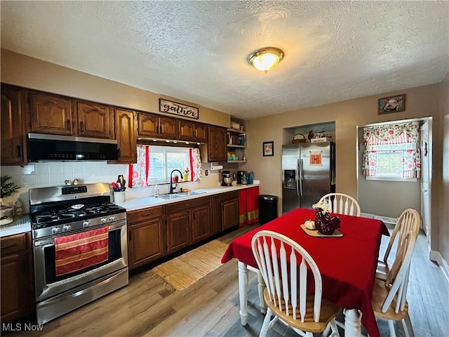 kitchen with sink, a textured ceiling, tasteful backsplash, light hardwood / wood-style floors, and stainless steel appliances