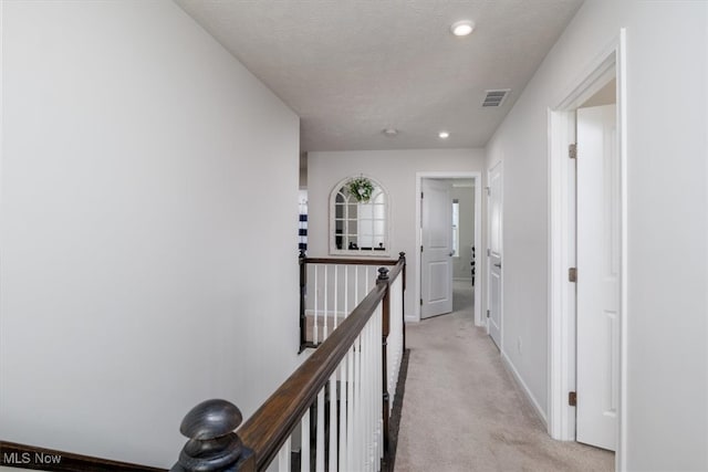 hall with a textured ceiling and light colored carpet