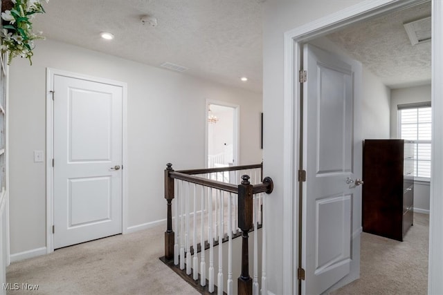 corridor with light carpet and a textured ceiling