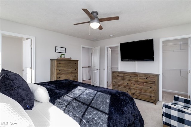 carpeted bedroom featuring a walk in closet, a textured ceiling, a closet, and ceiling fan