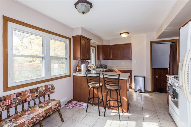 kitchen with white gas range, light tile patterned floors, sink, a breakfast bar, and kitchen peninsula