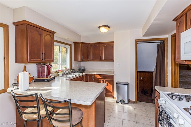 kitchen featuring light tile patterned flooring, sink, kitchen peninsula, a kitchen breakfast bar, and white appliances