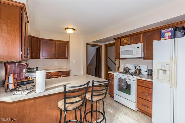 kitchen with kitchen peninsula, white appliances, light tile patterned floors, and a kitchen breakfast bar