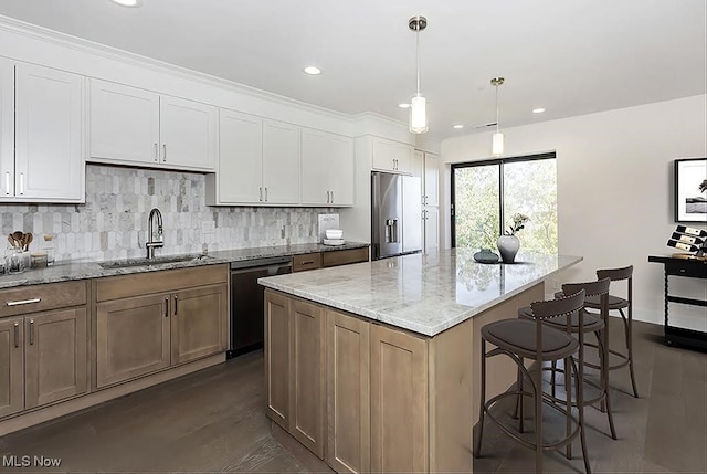 kitchen with sink, a kitchen island, hanging light fixtures, stainless steel appliances, and white cabinets