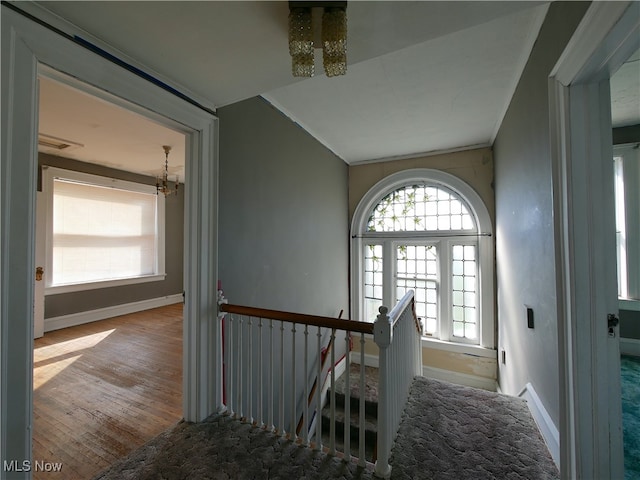 hallway with an inviting chandelier, ornamental molding, wood-type flooring, and vaulted ceiling