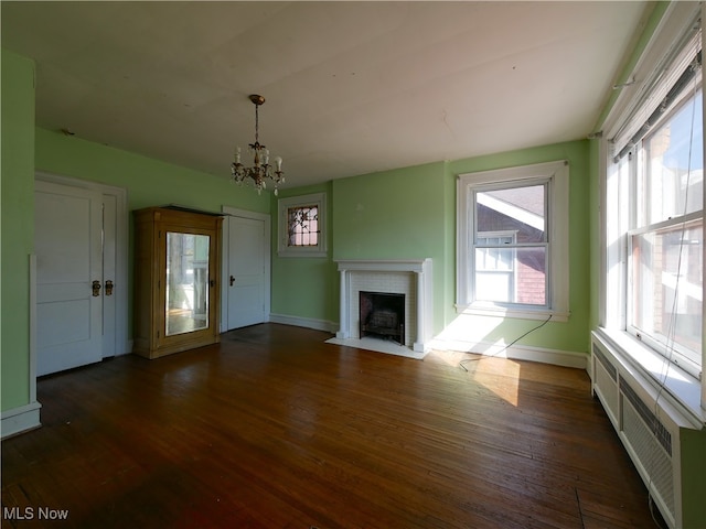 unfurnished living room with radiator heating unit, dark hardwood / wood-style flooring, a chandelier, and a brick fireplace