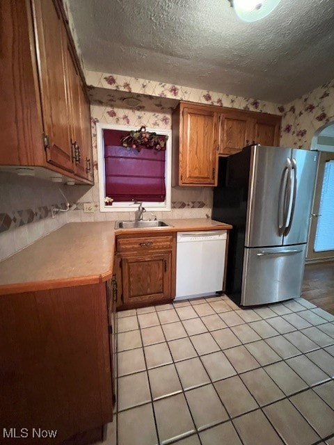 kitchen featuring sink, a textured ceiling, white dishwasher, stainless steel refrigerator, and light tile patterned floors