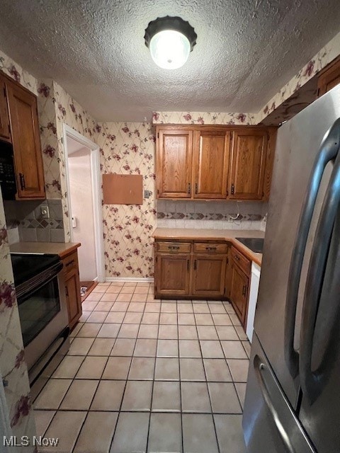 kitchen with stainless steel fridge, black electric range, a textured ceiling, and light tile patterned floors