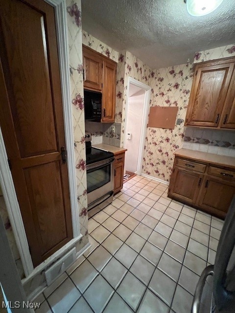 kitchen with a textured ceiling, stainless steel electric range, and light tile patterned floors