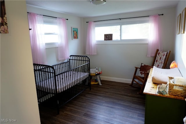 bedroom featuring dark wood-type flooring, multiple windows, and a crib