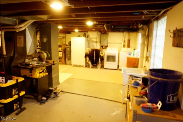 basement featuring electric panel, washing machine and clothes dryer, and white refrigerator