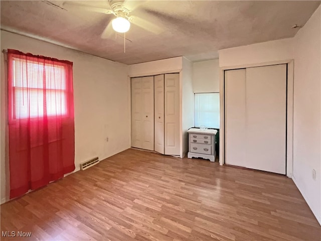 unfurnished bedroom with ceiling fan, multiple closets, and hardwood / wood-style floors