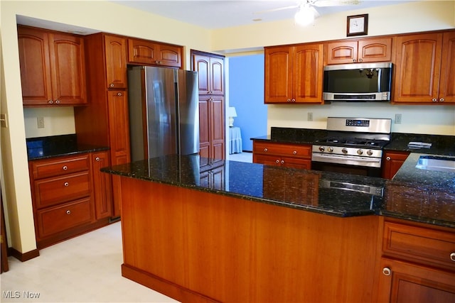 kitchen with appliances with stainless steel finishes, dark stone counters, and ceiling fan