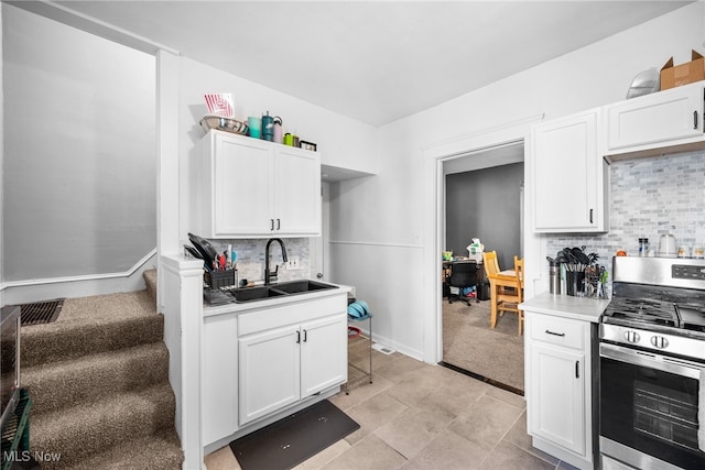 kitchen featuring decorative backsplash, white cabinetry, stainless steel stove, light colored carpet, and sink