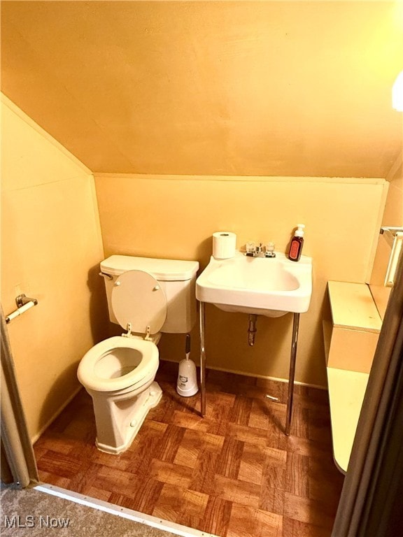 bathroom featuring sink, toilet, vaulted ceiling, and parquet floors