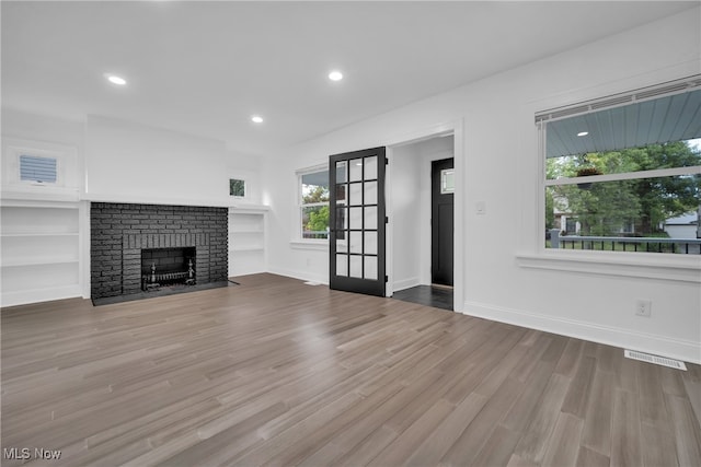 unfurnished living room with built in shelves, light wood-type flooring, and a fireplace