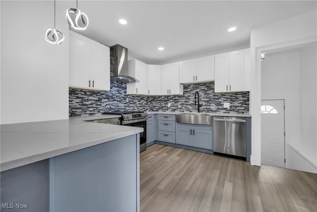 kitchen featuring sink, wall chimney exhaust hood, appliances with stainless steel finishes, decorative light fixtures, and white cabinetry