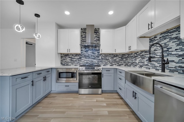 kitchen with light wood-type flooring, stainless steel appliances, wall chimney range hood, pendant lighting, and white cabinetry