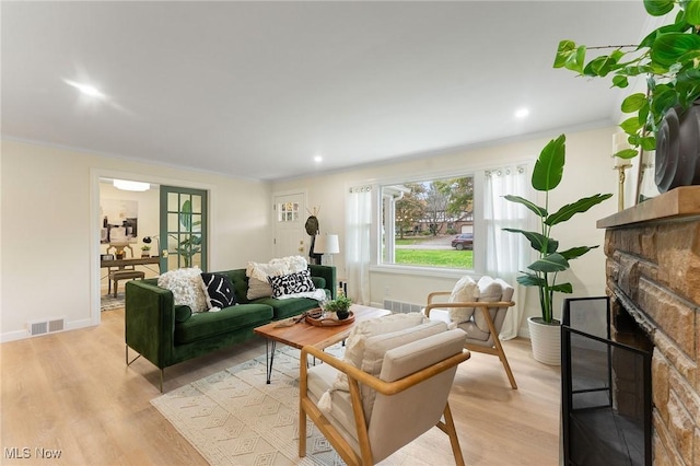 living room featuring light wood-type flooring, a stone fireplace, and crown molding