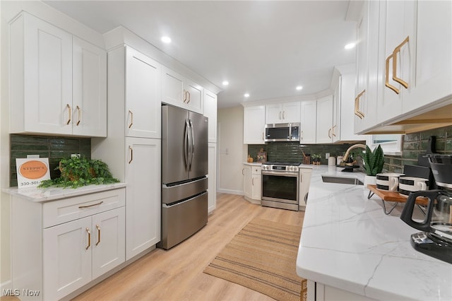 kitchen featuring light stone countertops, sink, appliances with stainless steel finishes, white cabinets, and light wood-type flooring