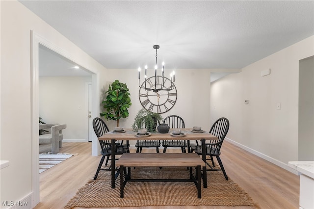 dining area featuring a notable chandelier, light wood-type flooring, and a textured ceiling