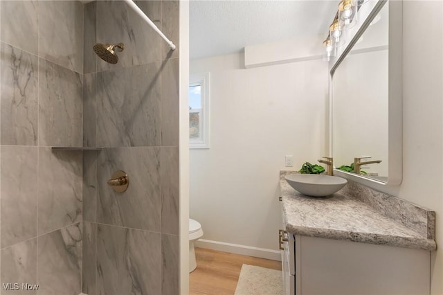 bathroom featuring vanity, hardwood / wood-style flooring, toilet, a textured ceiling, and a tile shower