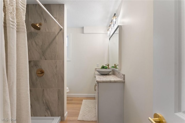 bathroom featuring a textured ceiling, vanity, wood-type flooring, and tiled shower