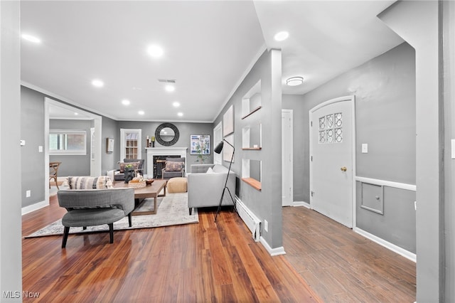 living room featuring wood-type flooring, ornamental molding, and a baseboard heating unit