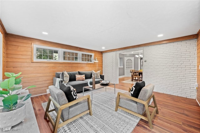 living room featuring a notable chandelier, brick wall, wood-type flooring, and wooden walls