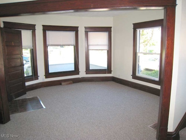 empty room featuring beam ceiling, a healthy amount of sunlight, and carpet flooring