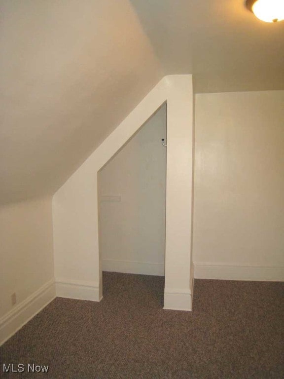 bonus room with dark carpet and vaulted ceiling