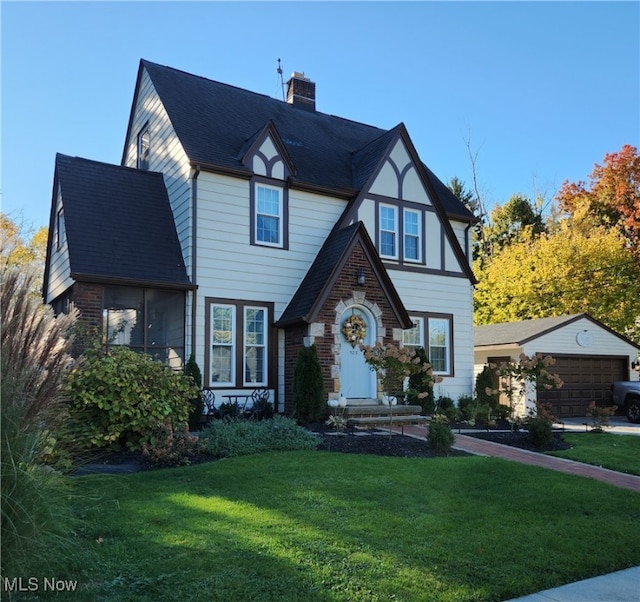 english style home with a garage, a front lawn, and an outbuilding