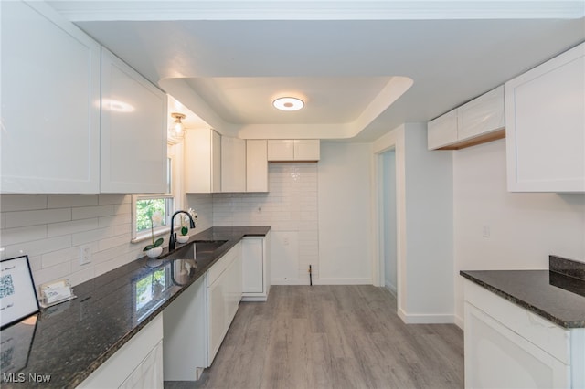 kitchen with white cabinets, sink, light wood-type flooring, and dark stone counters