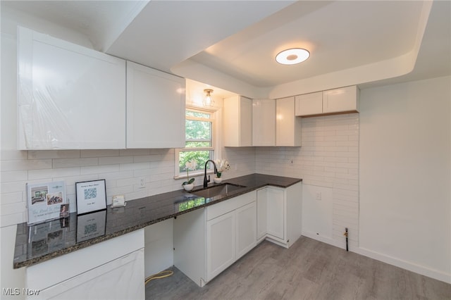 kitchen featuring tasteful backsplash, white cabinetry, light wood-type flooring, dark stone countertops, and sink