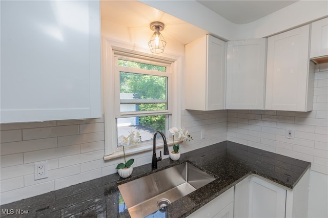 kitchen featuring white cabinets, dark stone countertops, sink, and backsplash