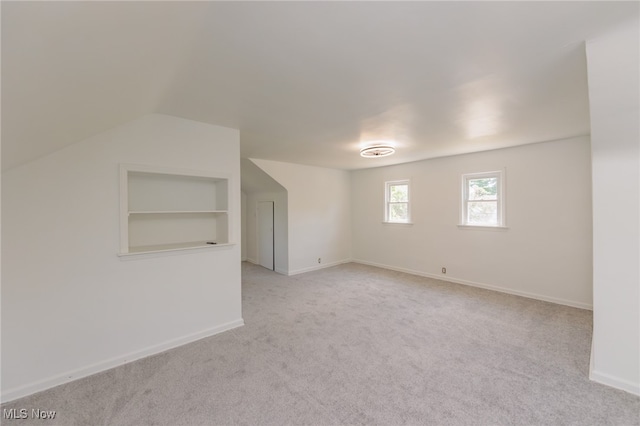 additional living space with vaulted ceiling, light carpet, and built in shelves