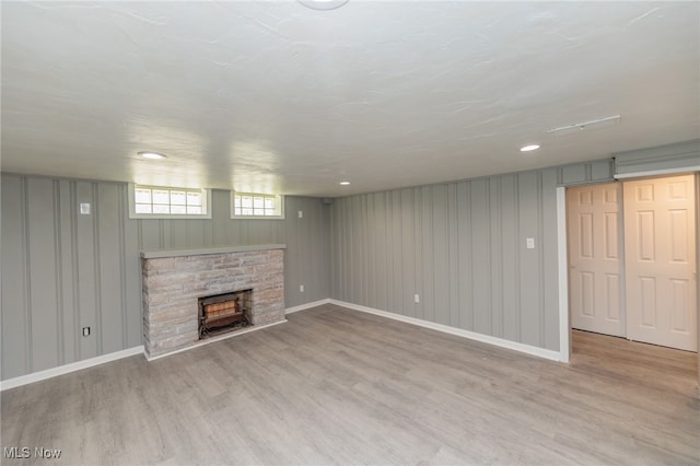 basement featuring a stone fireplace and light wood-type flooring