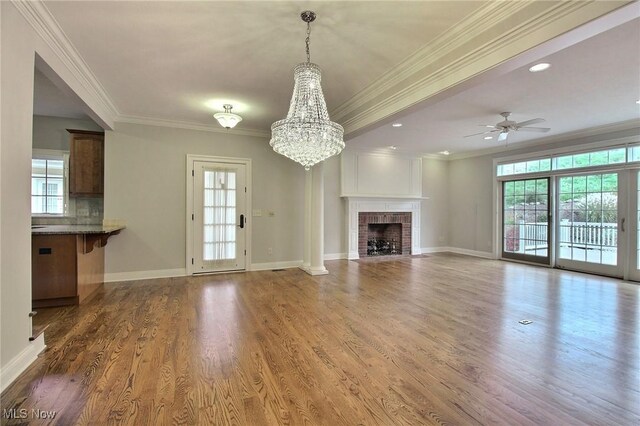 unfurnished living room featuring dark wood-type flooring, crown molding, a fireplace, and ceiling fan with notable chandelier