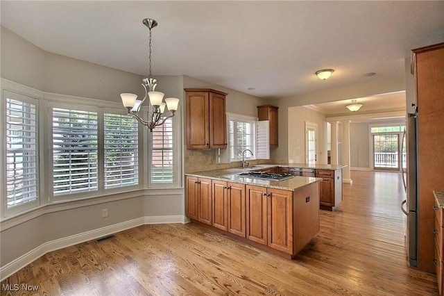 kitchen with sink, decorative light fixtures, kitchen peninsula, stainless steel appliances, and light hardwood / wood-style floors