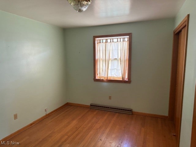 unfurnished room with a baseboard heating unit and light wood-type flooring