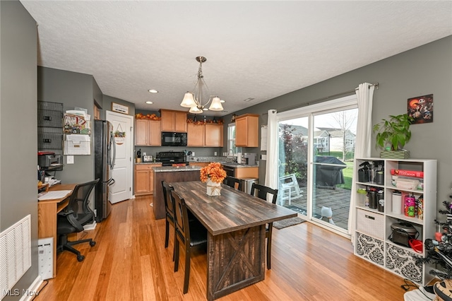 dining area featuring light hardwood / wood-style flooring, a textured ceiling, and a notable chandelier