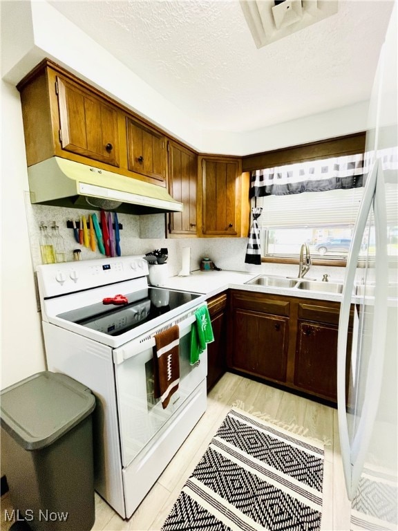 kitchen with decorative backsplash, a textured ceiling, light wood-type flooring, white range with electric stovetop, and sink