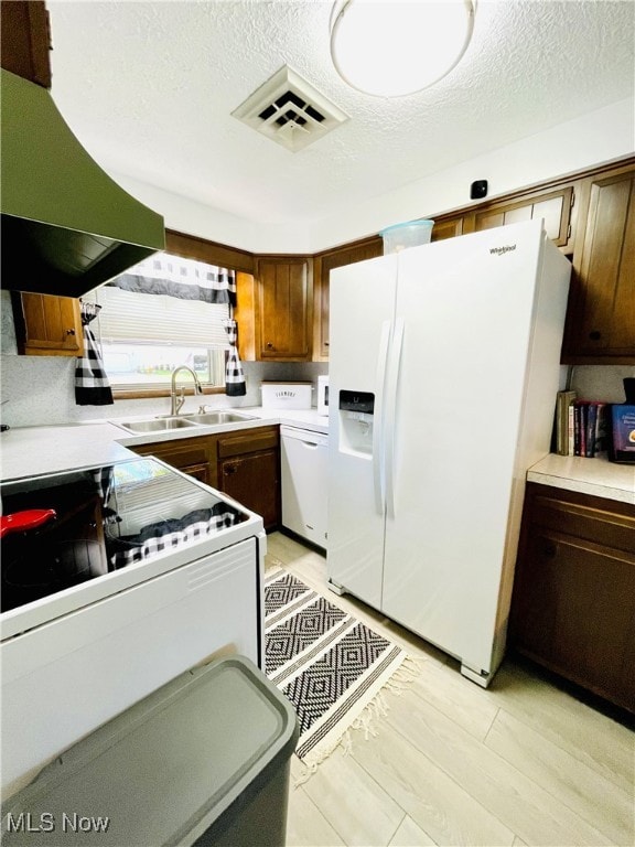 kitchen with a textured ceiling, sink, range hood, and white appliances