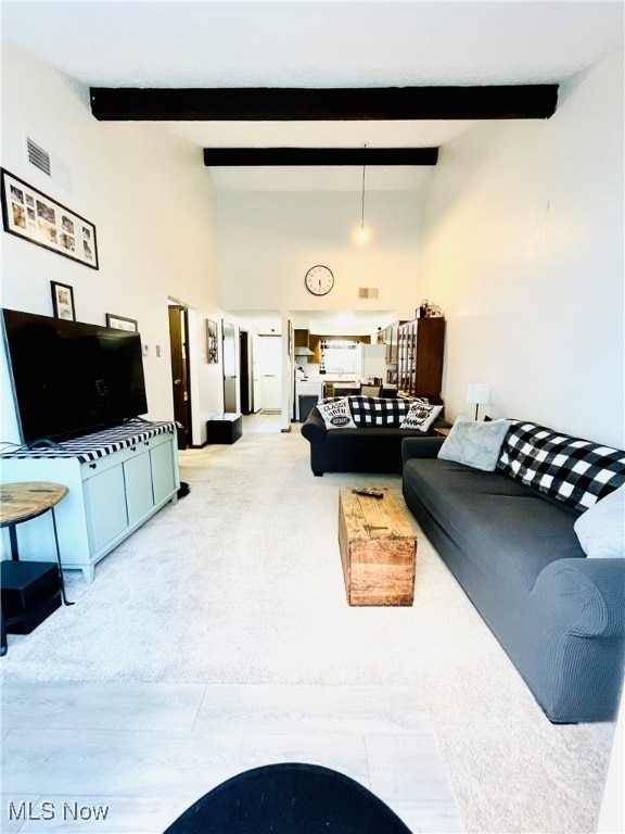 living room with beam ceiling, a high ceiling, and light carpet