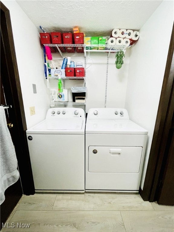 laundry room with independent washer and dryer, a textured ceiling, and light wood-type flooring