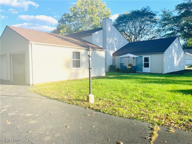 view of side of property featuring a garage, central air condition unit, and a lawn