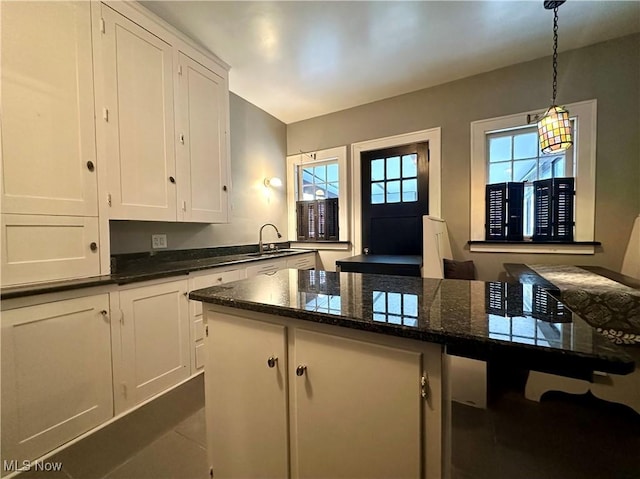 kitchen with sink, a kitchen island, dark stone countertops, pendant lighting, and white cabinets