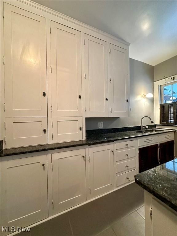 kitchen featuring tile patterned flooring, dark stone countertops, white cabinetry, and sink