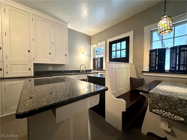 kitchen with a breakfast bar, sink, hanging light fixtures, dark stone countertops, and white cabinetry